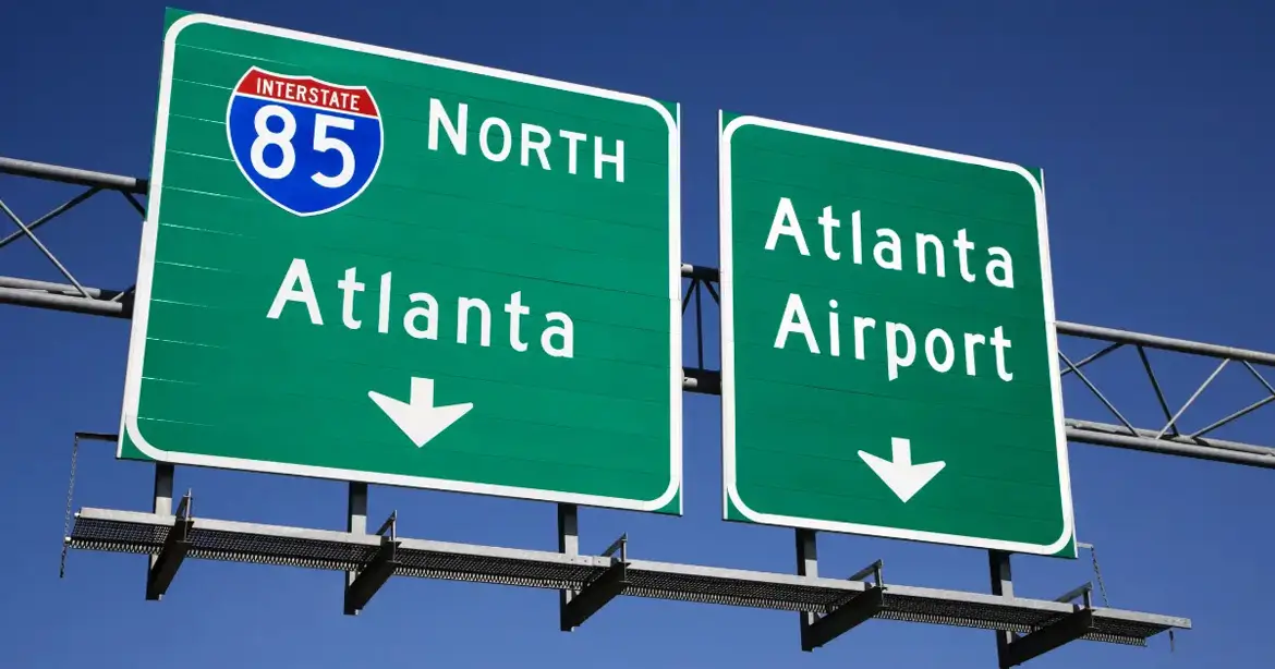Two green highway signs against a clear blue sky. The left sign indicates Interstate 85 North towards Atlanta, and the right sign points to Atlanta Airport.